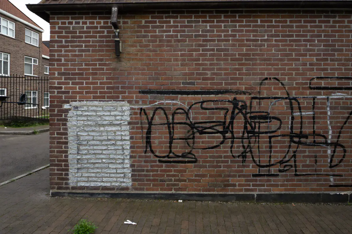 Spuitverfkrabbels op de onderkant van een bakstenen zijmuur, links een overgeverfd stuk