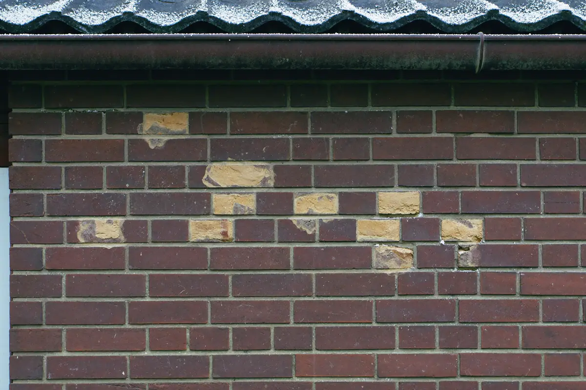Bakstenen met afgesprongen buitenkant en brokkelende voegen na vorstschade onderaan een gevel