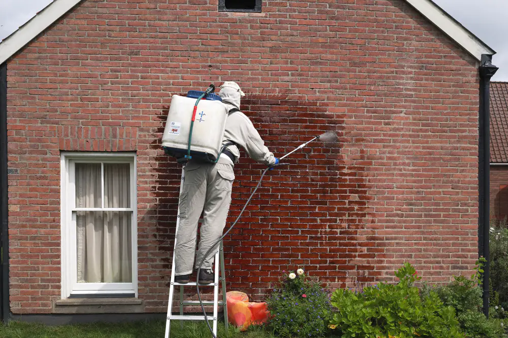 Een kleurloos waterafstotend middel wordt met lage druk op een droge bakstenen zijgevel gespoten